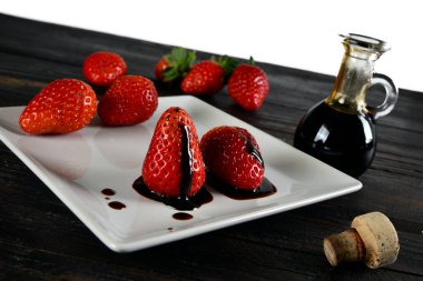 Bir fincan tabağında Modenese balzamik sirkesi ve etrafında çilek ve geleneksel balzamik sirke şişesi olan çilekler. 