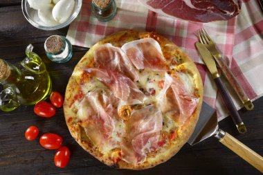 Taze pişmiş çiğ jambonlu pizza ve ahşap bir masaya konmuş mozzarella domatesi. 