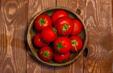 Fresh tomatoes in a plate on a wooden background. Top view