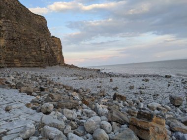 Kıyı sahnesi: dramatik uçurumlar, sahil, deniz ve gökyüzü.
