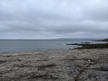 Okyanus dalgaları ve dramatik gökyüzü ile sakin bir sahil. Moelfre, Kuzey Galler.