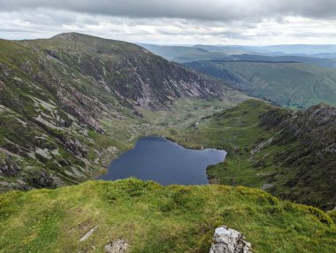 Sakin bir gölü ve bulutlu bir gökyüzünün altındaki yemyeşil tepeleri olan bir dağ sırasının nefes kesici manzarası..