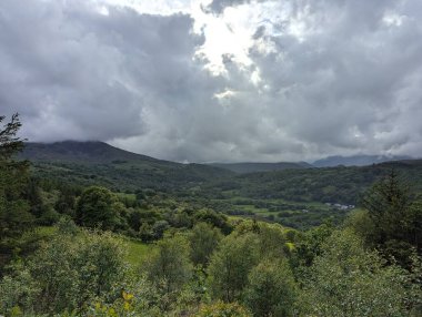 Yoğun ağaçları ve yuvarlanan tepeleri olan yemyeşil bir vadi üzerinde dramatik bulutlu bir gökyüzü. Manzara doğa görünümü.