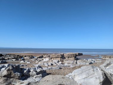 Mavi Anchor, Somerset, İngiltere 'de, sakin ve sakin bir kıyı sahnesini tasvir eden açık mavi bir gökyüzünün altında, dalgaların çekildiği Rocky sahili. Doğa, seyahat ve rahatlama kavramları için mükemmel..