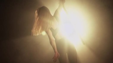 Young woman performs the acrobatic elements in the air hoop. Aerialist in on black background dark studio with backlight. For sports, acrobatic, circus school.