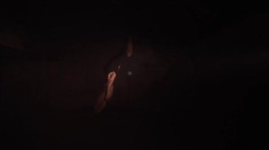Young woman performs the acrobatic elements in the air hoop. Aerialist in on black background dark studio with backlight. For sports, acrobatic, circus school.