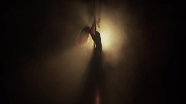 Young woman performs the acrobatic elements in the air hoop. Aerialist in on black background dark studio with backlight. For sports, acrobatic, circus school.