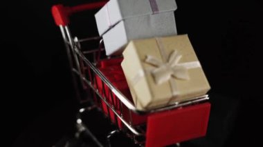 Hediye kutularının çeşitli renkleriyle dolu alışveriş arabası. Siyah arka plan.