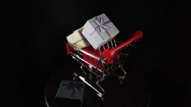 Hediye kutularının çeşitli renkleriyle dolu alışveriş arabası. Siyah arka plan.