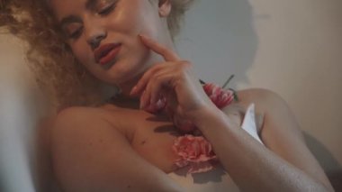 Kıvırcık saçlı çekici seksi kadın modern bir banyoda köpük ve çiçeklerle dolu bir küvette yatıyor. Güzellik konsepti.