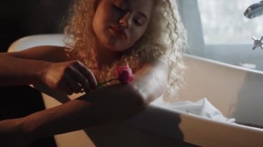 Kıvırcık saçlı çekici seksi kadın modern bir banyoda köpük ve çiçeklerle dolu bir küvette yatıyor. Güzellik konsepti.