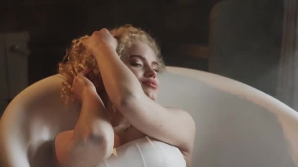 迷人的性感女人卷发躺在一个充满泡沫和鲜花的浴缸里 在一个现代化的浴室里 美的概念 — 图库视频影像