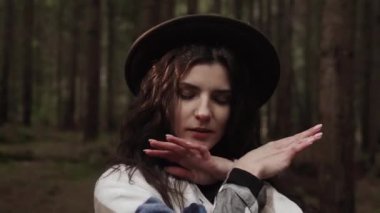 Sıcak bir battaniye ve şapkaya sarılı çekici bir kadın. Çam ormanında güneş ışığıyla poz veriyor. Dağ yolculuğu kavramı.