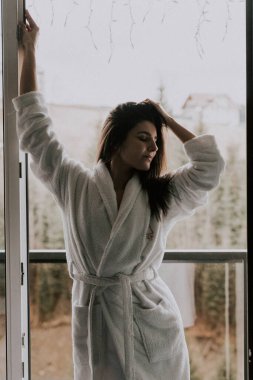 Beyaz bornozlu bir kadın kruvasan yer ve dağlardaki bir otelde kahve içer. Tatil konsepti.