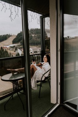 Beyaz bornozlu bir kadın kruvasan yer ve dağlardaki bir otelde kahve içer. Tatil konsepti.