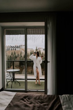 Beyaz bornozlu bir kadın kruvasan yer ve dağlardaki bir otelde kahve içer. Tatil konsepti.