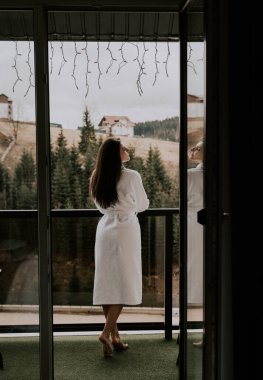 Beyaz bornozlu bir kadın kruvasan yer ve dağlardaki bir otelde kahve içer. Tatil konsepti.