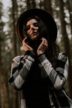 Çam ormanında poz veren şapkalı şık hippi kadın. Seyahat konsepti.