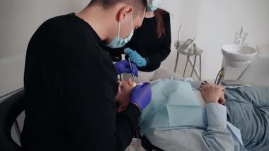 Diş kliniğinde koruyucu maskeli iki doktor hasta kıza hizmet ediyor. İş Dişçiliği. Sağlık ve Tıp Konsepti.