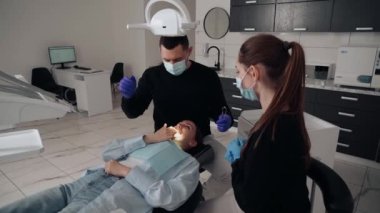 Diş kliniğinde koruyucu maskeli iki doktor hasta kıza hizmet ediyor. İş Dişçiliği. Sağlık ve Tıp Konsepti.