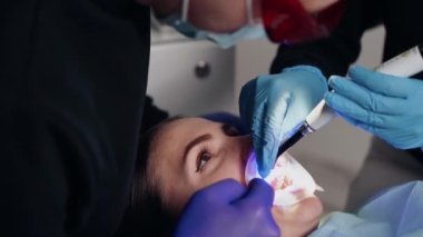 Diş kliniğinde koruyucu maskeli iki doktor hasta kıza hizmet ediyor. İş Dişçiliği. Sağlık ve Tıp Konsepti.