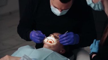 Diş kliniğinde koruyucu maskeli iki doktor hasta kıza hizmet ediyor. İş Dişçiliği. Sağlık ve Tıp Konsepti.