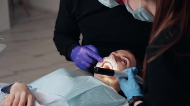 Diş kliniğinde koruyucu maskeli iki doktor hasta kıza hizmet ediyor. İş Dişçiliği. Sağlık ve Tıp Konsepti.