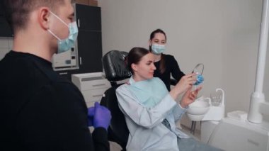 Diş kliniğinde koruyucu maskeli iki doktor hasta kıza hizmet ediyor. İş Dişçiliği. Sağlık ve Tıp Konsepti.