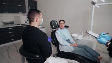 Diş kliniğinde koruyucu maskeli iki doktor hasta kıza hizmet ediyor. İş Dişçiliği. Sağlık ve Tıp Konsepti.