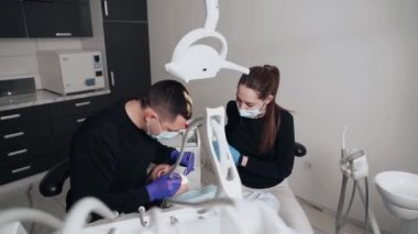 Diş kliniğinde koruyucu maskeli iki doktor hasta kıza hizmet ediyor. İş Dişçiliği. Sağlık ve Tıp Konsepti.