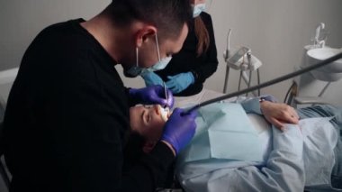 Diş kliniğinde koruyucu maskeli iki doktor hasta kıza hizmet ediyor. İş Dişçiliği. Sağlık ve Tıp Konsepti.