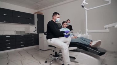 Diş kliniğinde koruyucu maskeli iki doktor hasta kıza hizmet ediyor. İş Dişçiliği. Sağlık ve Tıp Konsepti.