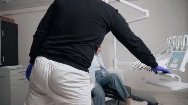 Diş kliniğinde koruyucu maskeli iki doktor hasta kıza hizmet ediyor. İş Dişçiliği. Sağlık ve Tıp Konsepti.