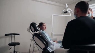 Diş kliniğinde koruyucu maskeli iki doktor hasta kıza hizmet ediyor. İş Dişçiliği. Sağlık ve Tıp Konsepti.