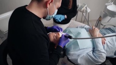 Diş kliniğinde koruyucu maskeli iki doktor hasta kıza hizmet ediyor. İş Dişçiliği. Sağlık ve Tıp Konsepti.