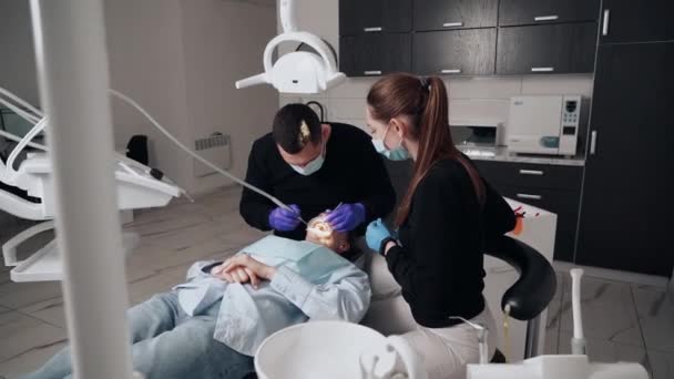 歯科医院の保護マスクの男と女の2人の医者は 患者の少女に奉仕します 歯医者だ 医療の概念 — ストック動画