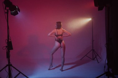 Stüdyoda renkli neon ışıklarıyla poz veren siyah elbiseli seksi kadın.