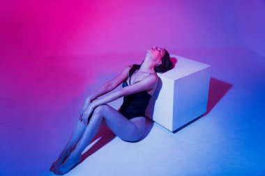 Stüdyoda renkli neon ışıklarıyla poz veren siyah elbiseli seksi kadın.