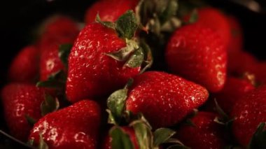 Siyah arka planda dönen çilekler. Taze, organik kırmızı çilekli çiğ vejetaryen yaz atıştırması.