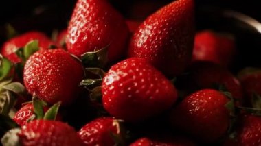 Siyah arka planda dönen çilekler. Taze, organik kırmızı çilekli çiğ vejetaryen yaz atıştırması.