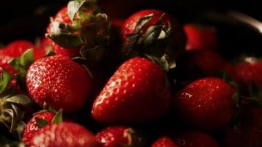 Siyah arka planda dönen çilekler. Taze, organik kırmızı çilekli çiğ vejetaryen yaz atıştırması.