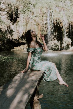 Bir dağ şelalesinin yanında poz veren turkuaz elbiseli güzel bir manken. Vahşi yaşam kavramı.