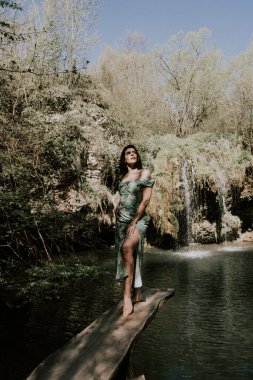 Bir dağ şelalesinin yanında poz veren turkuaz elbiseli güzel bir manken. Vahşi yaşam kavramı.