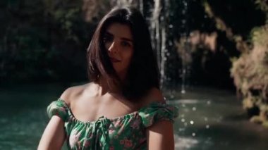 Bir dağ şelalesinin yanında poz veren turkuaz elbiseli güzel bir manken. Vahşi yaşam kavramı.