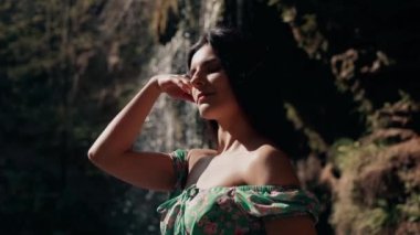 Bir dağ şelalesinin yanında poz veren turkuaz elbiseli güzel bir manken. Vahşi yaşam kavramı.