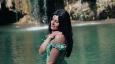 Bir dağ şelalesinin yanında poz veren turkuaz elbiseli güzel bir manken. Vahşi yaşam kavramı.