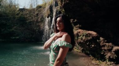 Bir dağ şelalesinin yanında poz veren turkuaz elbiseli güzel bir manken. Vahşi yaşam kavramı.