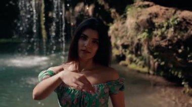 Bir dağ şelalesinin yanında poz veren turkuaz elbiseli güzel bir manken. Vahşi yaşam kavramı.