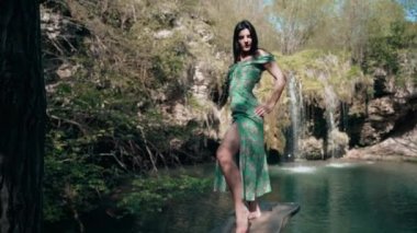 Bir dağ şelalesinin yanında poz veren turkuaz elbiseli güzel bir manken. Vahşi yaşam kavramı.