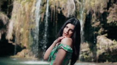 Bir dağ şelalesinin yanında poz veren turkuaz elbiseli güzel bir manken. Vahşi yaşam kavramı.